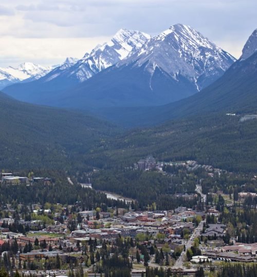 A breathtaking aerial view of Banff, AB, Canada showcasing majestic snow-capped mountains and lush greenery.