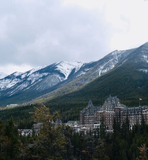 Scenic view of Banff Springs Hotel amidst snow-capped mountains and greenery.