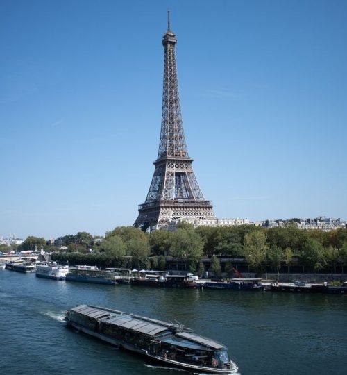 A scenic view of the Eiffel Tower and Seine River with boats on a sunny day in Paris, France.