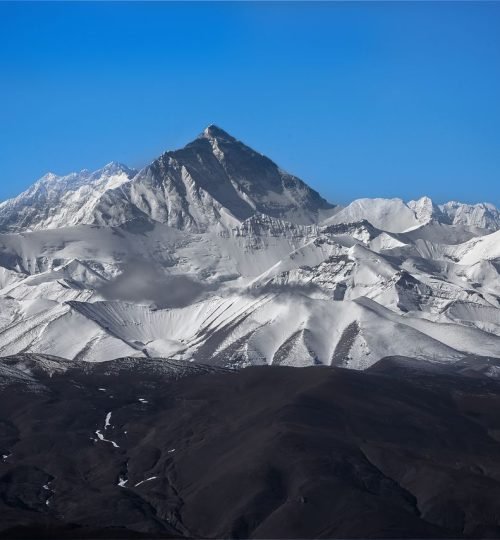 Stunning view of Mount Everest surrounded by snowy peaks under a clear blue sky.