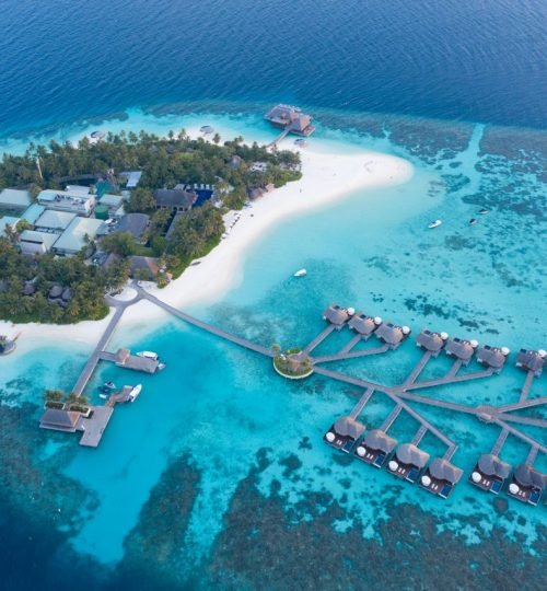 Stunning aerial view of a luxurious tropical island resort in the Maldives, featuring turquoise waters and overwater bungalows.